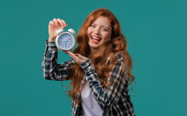 快乐的红发女人带着蓝色背景的闹钟。清晨，正确的生活规律，活在当下，珍惜生命的每一分钟，青春。图片下载