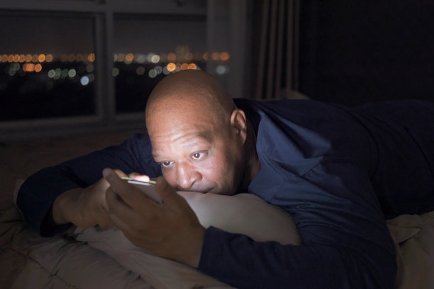 秃顶男子躺在家里的床上玩手机图片下载