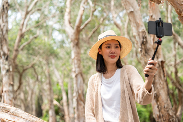 年轻的亚洲女性旅游视频博主独自拿着智能手机在森林里。假期周末快乐。迷人的女性旅行者在大自然中享受假期，在社交媒体上录制视频分享图片下载