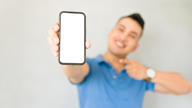 一名男子开心地指着手机，屏幕空白，背景是模糊的摄影棚图片下载