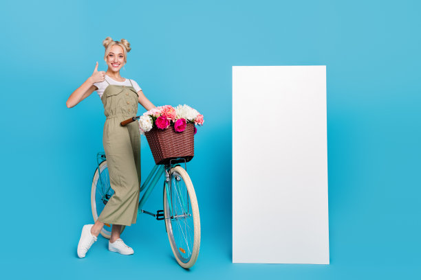 漂亮的金发女士的全尺寸照片与自行车拇指附近的促销穿t恤整体运动鞋孤立的蓝色背景图片下载