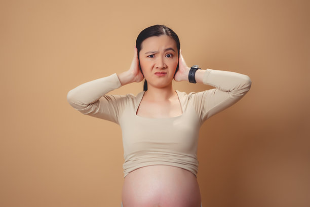 一名亚洲孕妇感到厌烦和烦恼，站在孤立的背景上捂着耳朵。图片下载