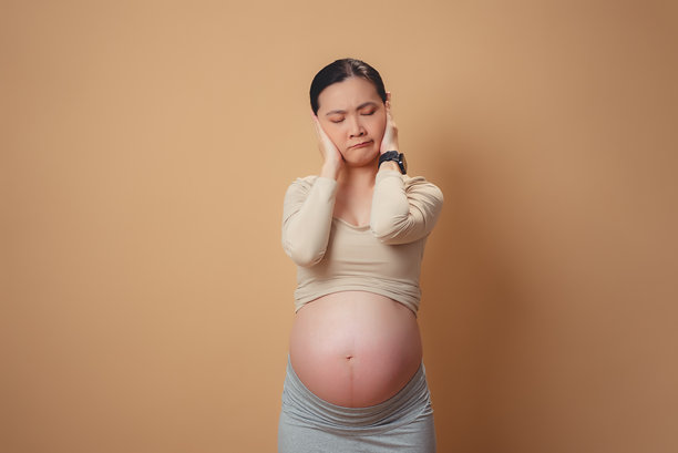 一名亚洲孕妇感到厌烦和烦恼，站在孤立的背景上捂着耳朵。图片下载