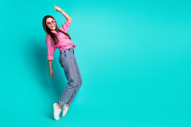 可爱的少女的全身照片太阳镜跳舞的脚尖有乐趣穿着时尚的粉红色服装孤立的青色背景图片下载