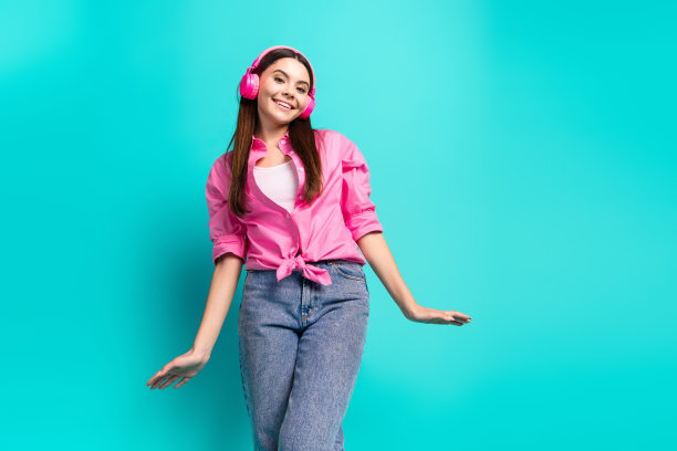 照片肖像迷人的少女耳机舞蹈有乐趣穿着时尚的粉红色衣服青色在蓝色的背景图片下载