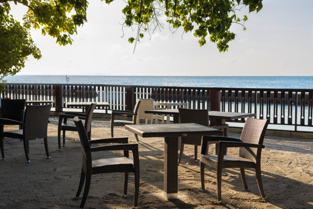 户外咖啡馆或餐馆里的空桌子和椅子被大海或海洋的树叶包围。等待访客。海浪和地平线的景色。放松的天堂。观光,旅游图片下载