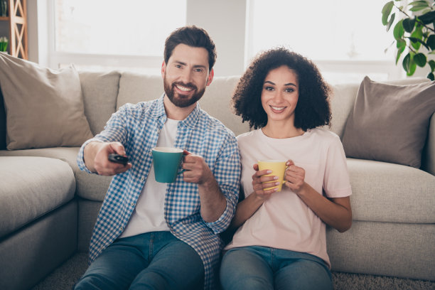 两个漂亮的年轻伙伴的照片空闲时间喝茶看电视周末现代公寓室内图片下载
