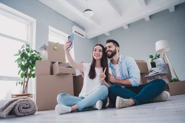 两个年轻伙伴的全尺寸照片自拍秀v-sign搬迁移动盒子包装新的现代公寓室内图片下载
