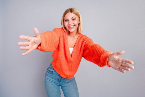 漂亮的年轻女孩手臂欢迎你橙色开衫孤立的灰色背景的照片图片下载