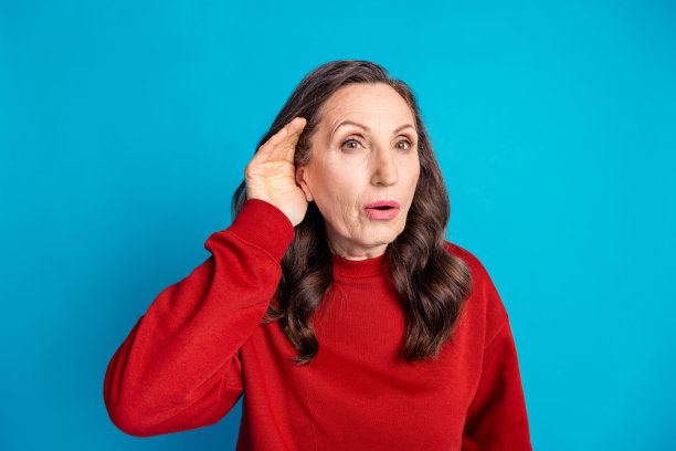 照片漂亮的老太太手臂耳朵偷听穿红色套头衫孤立的蓝色背景图片下载
