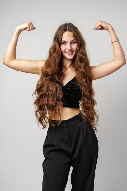 年轻的棕色长发的女人弯曲她的二头肌和微笑图片下载