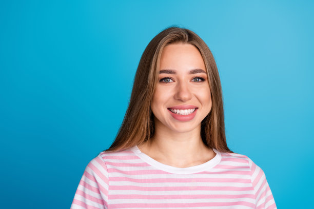 美丽的年轻女孩的照片肖像欢快的牙齿微笑穿着时髦的粉红色条纹衣服孤立的蓝色背景图片下载