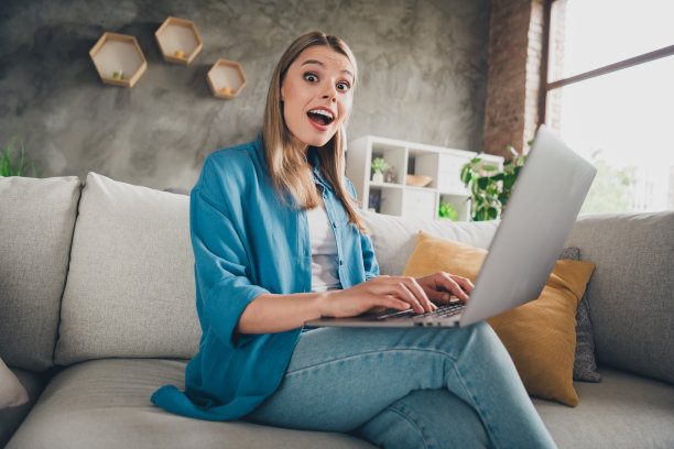 照片中的年轻美女穿着休闲的衣服，在家里用笔记本电脑在现代设计的客厅里网上购物图片下载