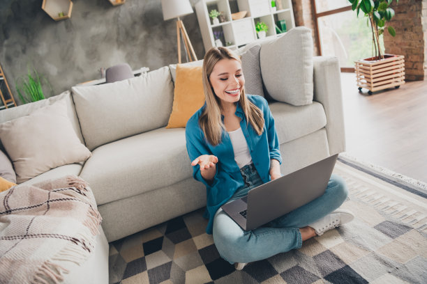 照片中，年轻开朗的女性穿着休闲装，正在工作的人力资源经理在家里用笔记本电脑在现代设计的客厅里招聘求职者图片下载