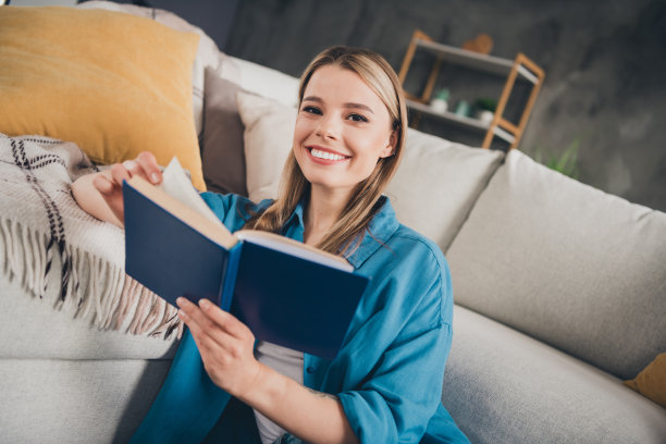 照片年轻迷人的家庭女士穿着蓝色休闲衬衫在室内阁楼现代设计公寓客厅独自坐着看书图片下载