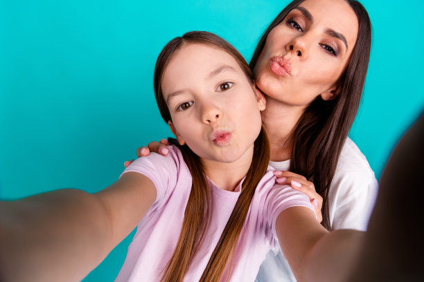 可爱的小女孩和妈妈拍视频自拍的照片，白色的时尚衣服被隔离在青色背景上图片下载