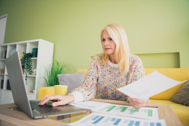 照片中漂亮的老妇人手持纸张，使用笔记本电脑，书桌，客厅，公寓，室内图片下载