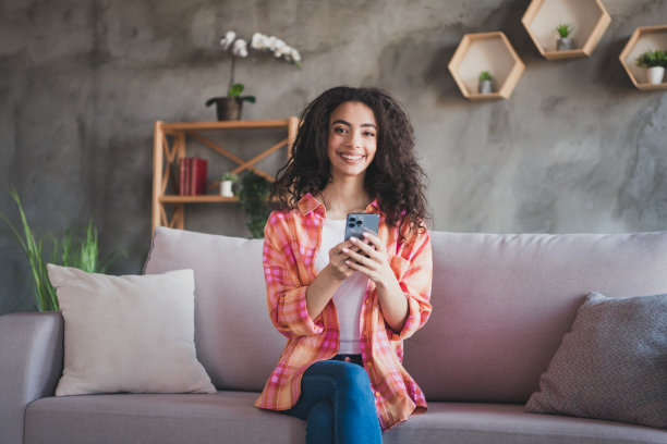 照片中闪亮可爱的女孩穿着白色格子衬衫，微笑着在房子里的公寓房间里发短信图片下载
