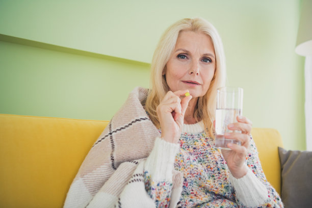 照片中漂亮的老妇人手持玻璃水丸，穿着套头衫，住在客厅公寓的室内图片下载