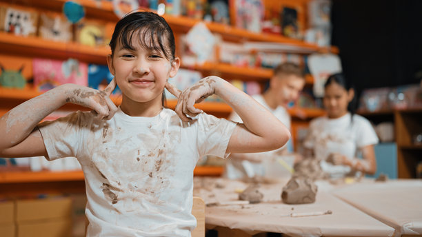 亚洲女孩在镜头前摆姿势，而不同的孩子在做粘土模型。启迪。图片下载