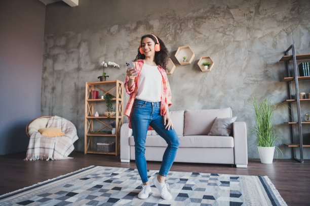 照片中闪亮可爱的女孩穿着白色格子衬衫，戴着耳机，在房子公寓房间里听着现代设备图片下载