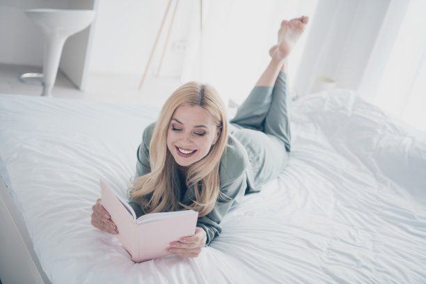 漂亮年轻女子的全尺寸照片躺在床上看书睡衣白色室内卧室公寓室内图片下载