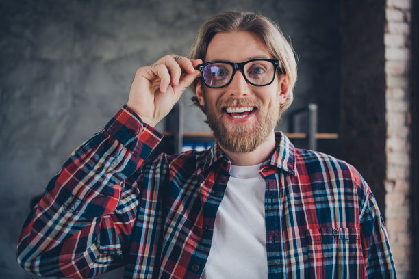 照片漂亮的年轻男性兴奋触摸眼镜穿格子衬衫舒适的现代办公室阁楼房间室内室内商人的工作空间图片下载