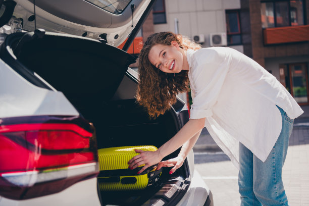 照片中的兴奋梦幻的女士把旅行箱汽车后备箱游客穿着白衬衫走在现代城市的城市街道图片下载