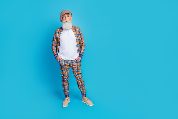 全身照片自信迷人的退休男子穿着格子西装站立双手口袋空空间孤立的蓝色背景图片下载