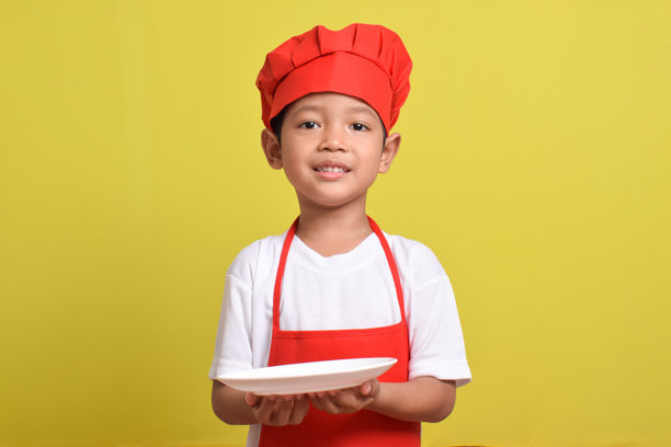 穿着红围裙的亚洲男孩。可爱的小厨师带着盘子图片下载