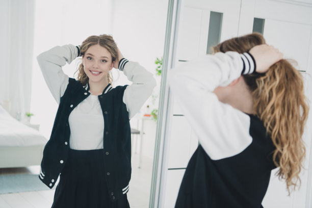 十几岁的金发可爱的女士的照片调整头发尾镜反射穿着时尚的制服寒冷的公寓卧室白光室内图片下载