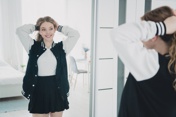 照片十几岁的金发甜美可爱的女士调整头发尾巴照镜子穿着时尚的制服寒冷的公寓卧室白光室内图片下载