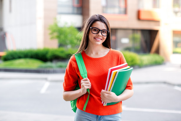 照片漂亮的青少年好心情的女孩拿着抄写书学生穿着红色的衣服走在城市公园外图片下载