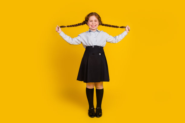 可爱的小女生的全身照片拉头发辫俏皮穿着时尚的制服孤立的黄色背景图片下载