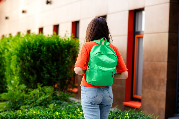 照片漂亮的青少年好心情的女孩后视图学生背包穿着红色的衣服走在城市公园外面图片下载