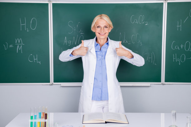 迷人漂亮的高级女学校教师的照片，穿着白色大褂，大拇指向上，孤立在绿色的纸板背景上图片下载