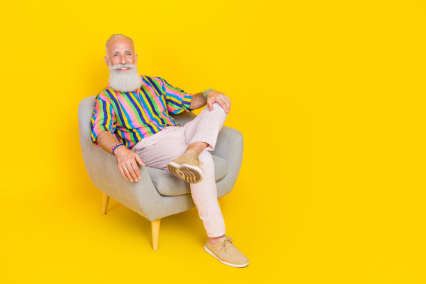 正能量老人的全尺寸照片，坐在扶手椅上，有好心情的空白空间和孤立的黄色背景图片下载