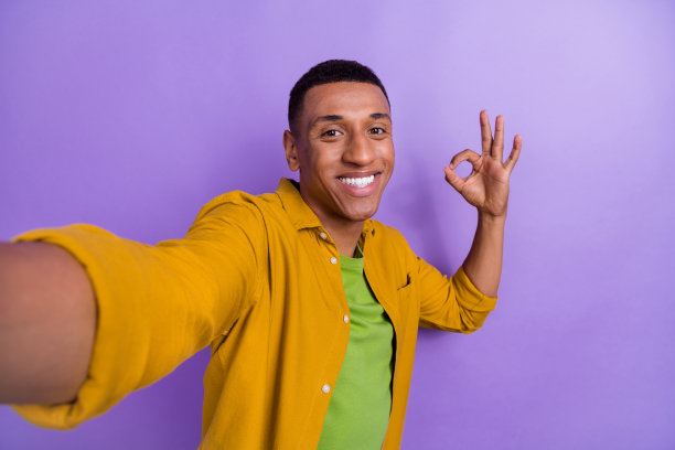 漂亮年轻人的照片肖像，视频记录自拍秀，ok符号穿着时尚的黄色衣服，孤立在紫色背景上图片下载