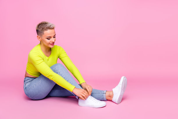 有魅力的年轻女子的全尺寸照片系鞋带试穿新的运动鞋穿着时尚的黄色服装孤立在粉红色的背景图片下载