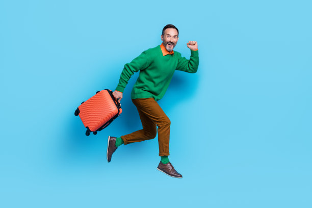成熟英俊男子的全身照片跑得很快，提着手提箱，穿着时尚的绿色服装，孤立在蓝色背景上图片下载