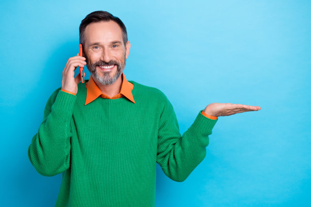 照片英俊的积极男子讲电话手臂手掌握空空间孤立的蓝色背景图片下载