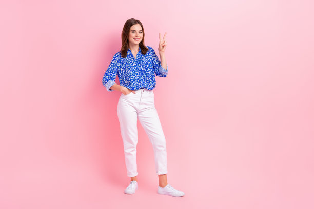 友好甜美的女人穿着蓝色衬衫的全身照片显示v字空空间孤立的粉红色背景图片下载