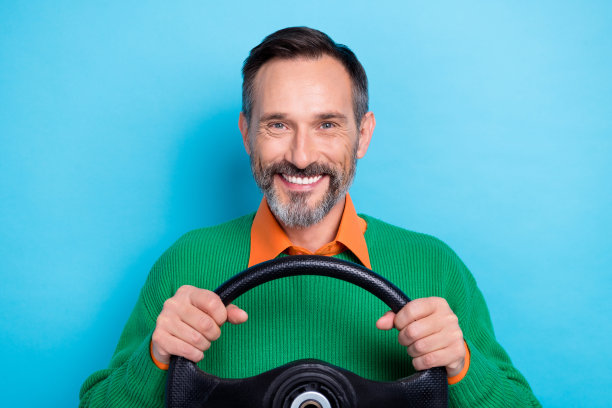 照片上的牙齿灿烂满意的微笑，成熟的老年灰胡子男子穿着套头衫抱着新车方向盘司机孤立的蓝色背景图片下载