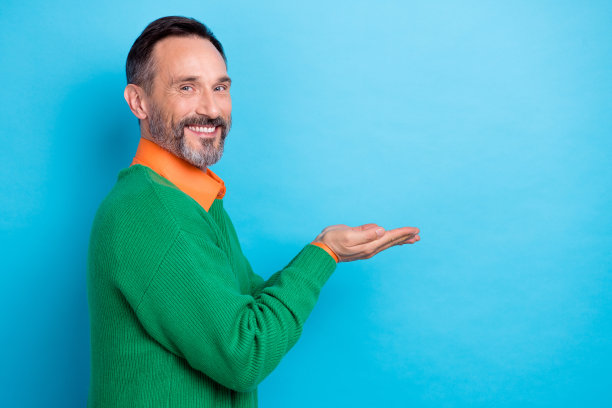 照片肖像中英俊的男子手持空空的空间产品宣传穿着时尚的绿色衣服孤立在蓝色的背景图片下载