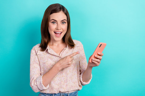 兴奋的漂亮女孩穿着粉红色的衬衫指着苹果三星现代小工具孤立的蓝绿色背景的照片图片下载
