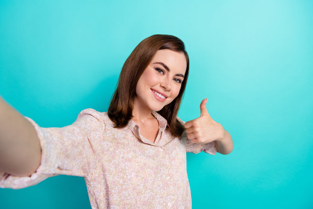 照片积极自信的女孩穿着粉红色的衬衫录制视频视频日志显示拇指向上孤立的蓝绿色背景图片下载