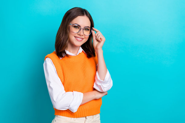 照片的好心情有趣的女人直发穿橙色马甲手触摸眼镜孤立在蓝绿色的背景图片下载