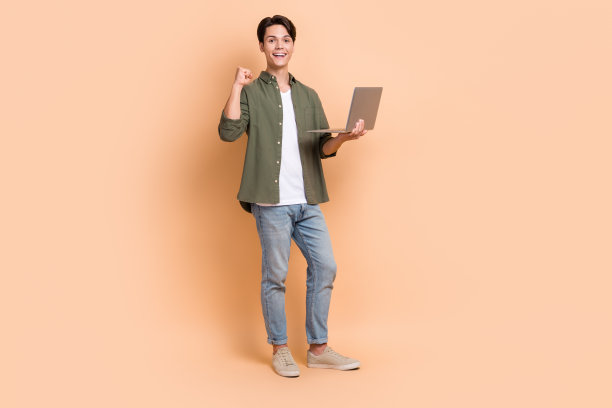 年轻男子自由职业IT程序员完成第一个代码举起拳头拿笔记本全身照图片下载