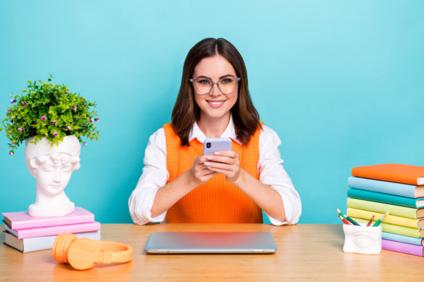 可爱迷人的聪明女士自由职业者的照片，穿着时尚的衣服，使用现代的小工具，坐在桌子上，在青色的背景上与世隔绝图片下载