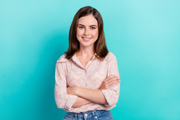 照片中，开朗自信的女孩穿着粉色衬衫，双臂交叉微笑，孤立的蓝绿色背景图片下载